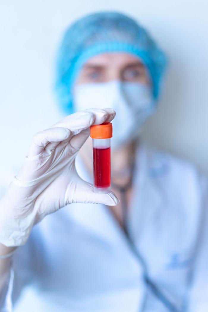 Healthcare worker holding a blood vial in a laboratory setting, wearing protective gear.