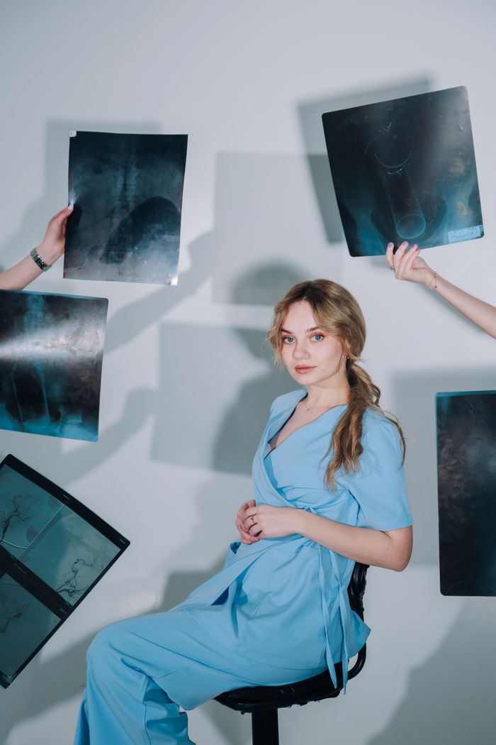 Female medical professional in blue scrubs examining X-ray images in a clinical setting.