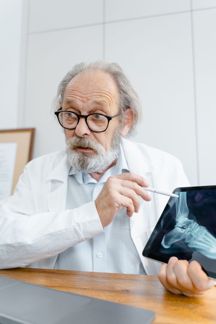 Senior male doctor explaining an X-ray image using a digital tablet indoors.