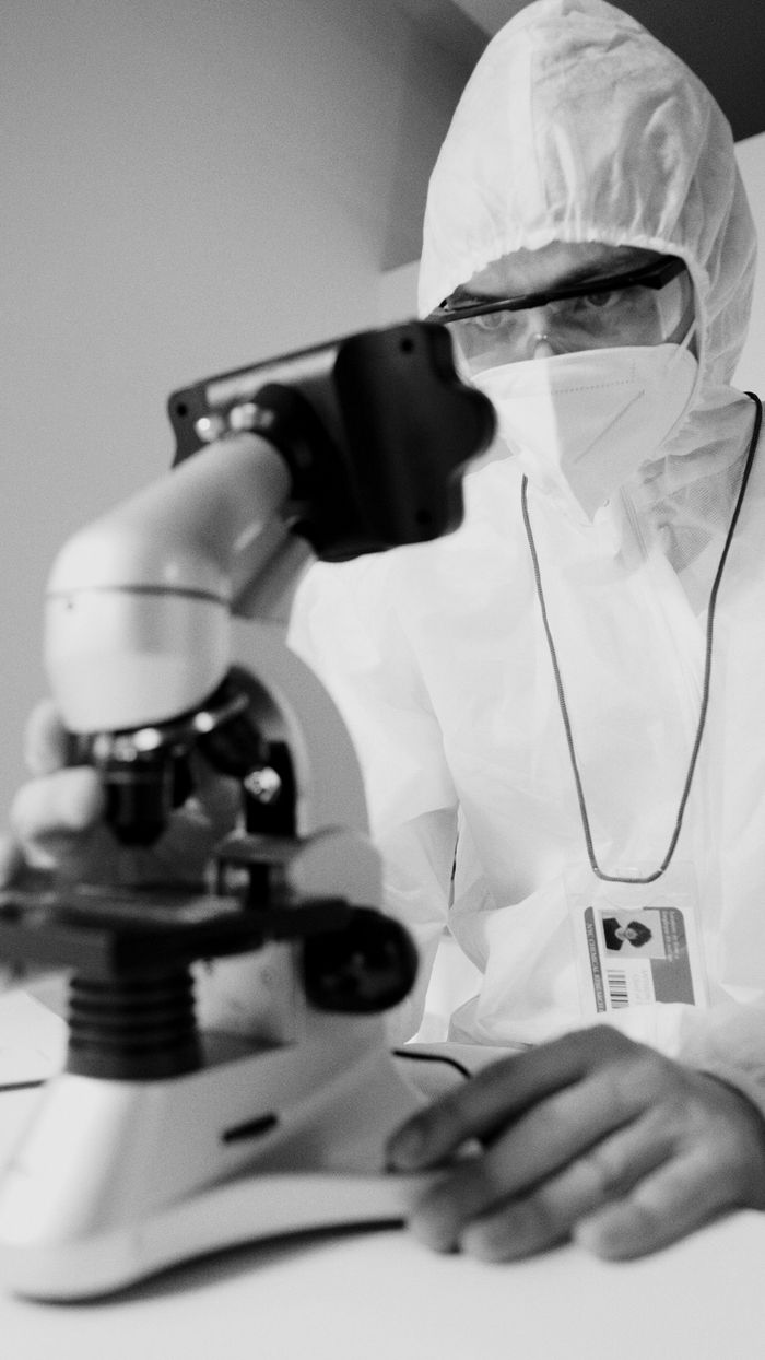Biochemist wearing PPE conducts research with microscope in lab